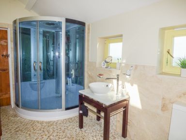 A bathroom with a curved glass shower cabin a freestanding sink on a wooden table and two windows at Humbleton Cottage in Haydon Bridge near Hexham
