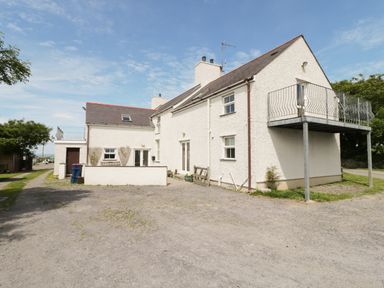 An exterior view of a white two-story house with chimneys balcony and gravel driveway at Bodegri Cottage Llanrhyddlad near Church Bay