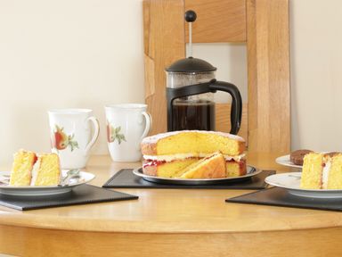 A wooden table with a Victoria sponge cake and two plates with cake slices two cups and a French press coffee pot at Bodegri Cottage in Llanrhyddlad near Church Bay