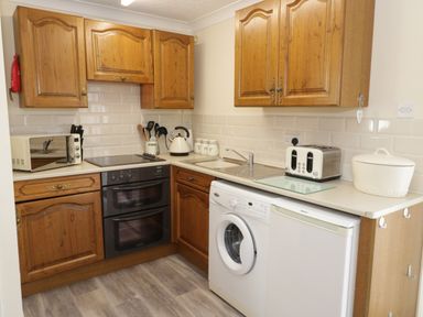A kitchen with wooden cabinets a washing machine a toaster a kettle and a bread bin at Bodegri Cottage in Llanrhyddlad near Church Bay