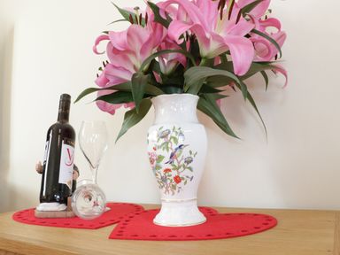 A white vase with pink flowers and a bottle of wine with two glasses on a wooden surface at Bodegri Cottage in Llanrhyddlad near Church Bay