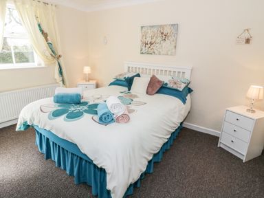 A bedroom with a bed covered in floral bedding towels on the bed two bedside tables with lamps and a window with curtains at Bodegri Cottage Llanrhyddlad near Church Bay