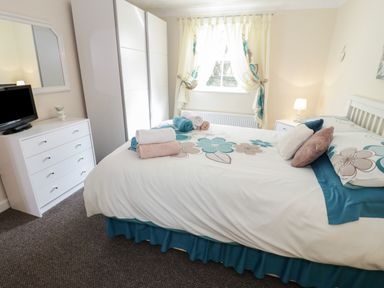 A bedroom with a bed folded towels a dresser with a television wardrobe and a window at Bodegri Cottage in Llanrhyddlad near Church Bay