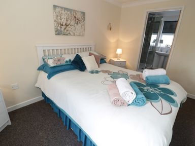 A bedroom with a bed and folded towels by a en suite bathroom at Bodegri Cottage in Llanrhyddlad near Church Bay