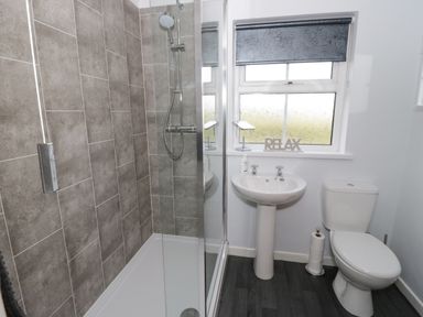 A bathroom with a shower, sink, toilet, and window with blinds at Bodegri Cottage in Llanrhyddlad near Church Bay
