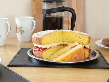 A slice of Victoria sponge cake with jam and cream on a plate beside a coffee press and two cups at Bodegri Cottage in Llanrhyddlad near Church Bay