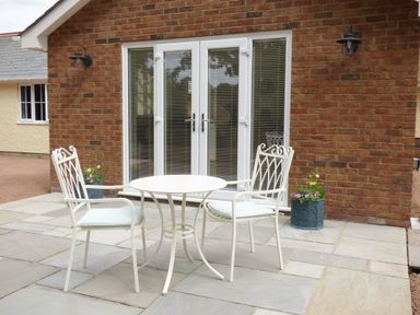 A patio with a round metal table and two chairs in front of glass doors at The Hideaway in Verwood