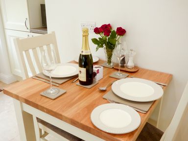 A dining table set for two with plates glasses a bottle of prosecco and red roses at The Hideaway in Verwood