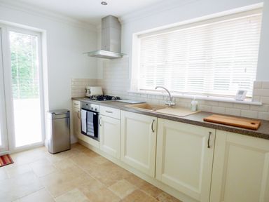A kitchen with cream cabinets a countertop with a sink stove oven and a window with blinds at The Hideaway in Verwood