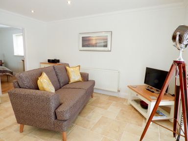 A living room with a sofa pillows television and a tripod lamp at The Hideaway in Verwood