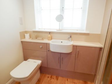 A bathroom with a toilet sink cabinets and a window with blinds at The Hideaway in Verwood
