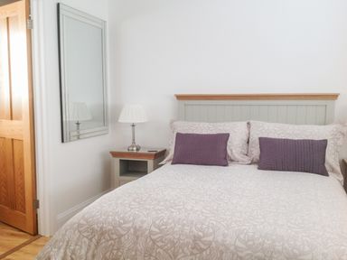 A bedroom with a bed featuring a headboard two pillows and two cushions beside a bedside table with a lamp and a wall mirror at The Hideaway in Verwood