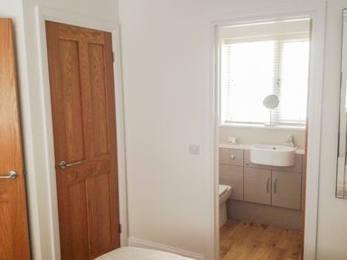 A view of a bathroom with a sink and cabinets through a doorway from a room with wooden doors and white walls at The Hideaway in Verwood