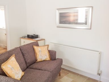 A room with a patterned couch with yellow pillows beside a white radiator and a small cabinet with a radio on top at The Hideaway in Verwood