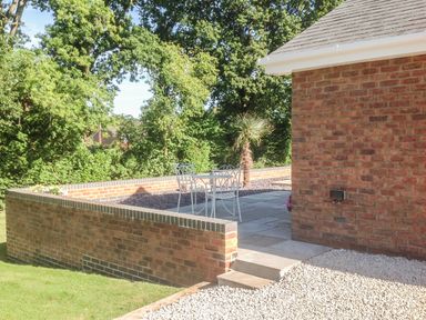 An outdoor patio area with metal chairs and a table next to a brick wall and a building at The Hideaway in Verwood