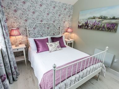 A bedroom with a white metal bed frame purple pillows floral wallpaper and a landscape painting at Stoney-Brook Lodge Bedlam near Ludlow