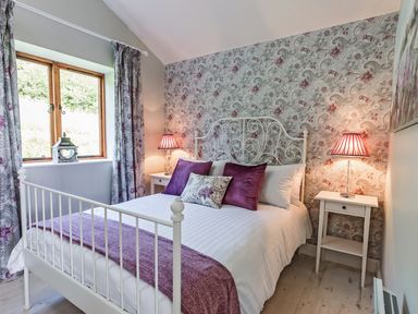 A bedroom with a white metal bed frame purple pillows and patterned wallpaper at Stoney-Brook Lodge in Bedlam near Ludlow