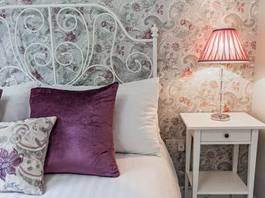 A bedroom with white metal bed frame purple and patterned pillows and a white bedside table with a lamp at Stoney-Brook Lodge Bedlam near Ludlow