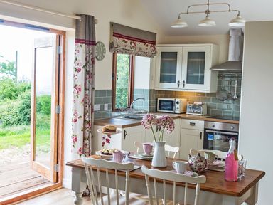 A kitchen with a wooden table set for tea and an open door leading outside at Stoney-Brook Lodge in Bedlam near Ludlow