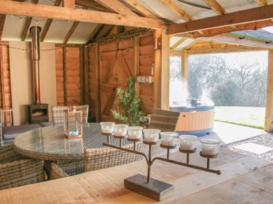 A wooden cabin interior with a round glass table and wicker chairs a metal candle holder on a wooden table a small wood stove and an outdoor hot tub at Stoney-Brook Lodge in Bedlam near Ludlow