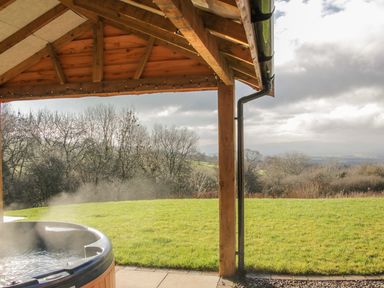 An outdoor covered patio with a hot tub overlooking a grassy lawn and trees at Stoney-Brook Lodge in Bedlam near Ludlow