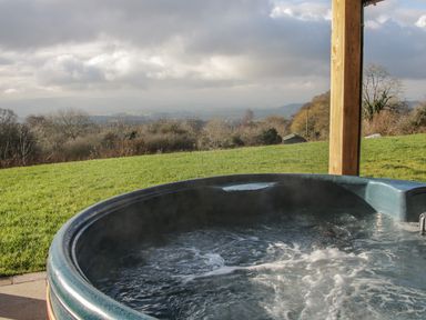 A bubbling hot tub on a patio with a grassy field and cloudy sky at Stoney-Brook Lodge in Bedlam near Ludlow