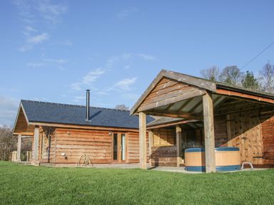 Exterior view of a wooden lodge with a covered hot tub on a grassy lawn at Stoney-Brook Lodge in Bedlam near Ludlow
