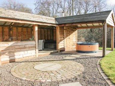 An outdoor wooden structure with seating area and hot tub on gravel and patio at Stoney-Brook Lodge in Bedlam near Ludlow