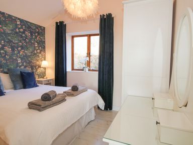 A bedroom with a bed holding folded towels bedside table with lamp floral wallpaper and a dresser with a mirror at Stoney-Brook Lodge in Bedlam near Ludlow