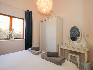 A bedroom with a bed holding folded towels a white wardrobe a dressing table with an oval mirror and a window with dark curtains at Stoney-Brook Lodge in Bedlam near Ludlow