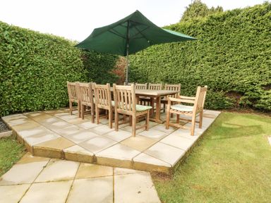 An outdoor patio with a wooden dining table surrounded by wooden chairs and a large green umbrella at Bay View in Benllech