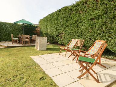 A garden with wooden chairs and a table with a green umbrella and a barbecue area at Bay View in Benllech