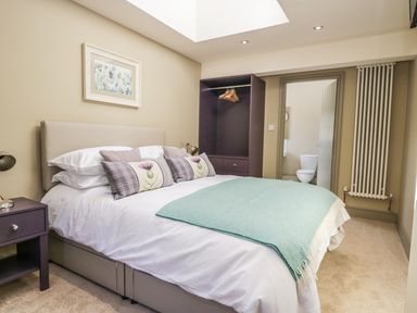 A bedroom with a double bed a bedside table an open wardrobe and an en suite bathroom at Providence Cottage in Easingwold