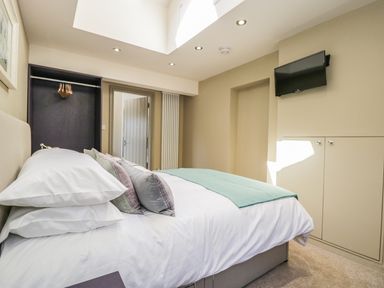 A bedroom with a bed pillows wall-mounted television open closet and beige walls at Providence Cottage in Easingwold