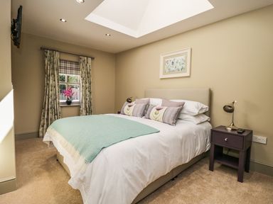 A bedroom with a bed with pillows and a green throw next to a window with floral curtains at Providence Cottage in Easingwold
