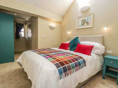 A bedroom with a bed with colorful pillows and a blanket and a teal side table at Providence Cottage in Easingwold