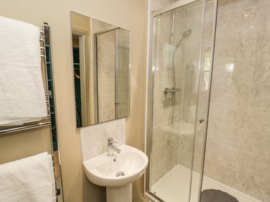 A bathroom with a sink and mirror next to a glass shower enclosure at Providence Cottage in Easingwold