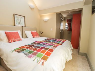 A bedroom with two single beds joined together with colorful blanket and red cushions at Providence Cottage in Easingwold