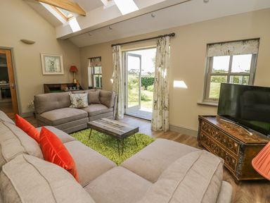 A living room with beige sofas a wooden coffee table green rug and a television on a wooden cabinet at Providence Cottage in Easingwold