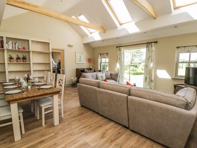 A living room with a dining table set for six people a bookshelf two sofas a television and skylight windows at Providence Cottage in Easingwold