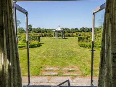 A garden view with a lawn and a gazebo seen through open glass doors at Providence Cottage in Easingwold