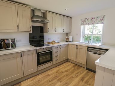 A kitchen with beige cabinets a built-in oven a microwave a dishwasher a sink under a window and a wooden floor at Providence Cottage in Easingwold