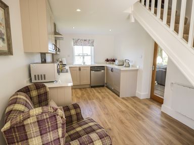 A kitchen with a plaid armchair a microwave dishwasher and a window under stairs at Providence Cottage in Easingwold