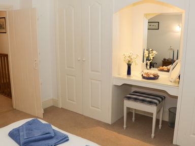 A bedroom corner with a dressing table mirror stool and towels on a bed at Coachmans Cottage in Witherslack