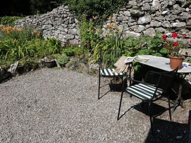 An outdoor seating area with two chairs and a table with a potted plant next to a stone wall and plants