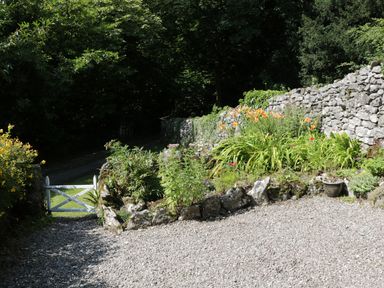 A garden with flowers a stone wall and a gravel path at Coachmans Cottage in Witherslack
