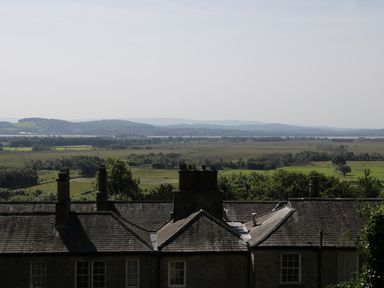 A rural landscape with fields trees and hills beyond rooftops of stone buildings with chimneys at Coachmans Cottage in Witherslack
