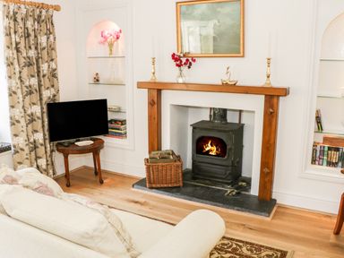 A living room with a wood burning stove fireplace a television on a wooden table and bookshelves at Coachmans Cottage in Witherslack