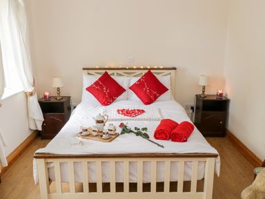 A bedroom with a bed with red pillows two rolled towels a rose and tea set on the bed two bedside tables with lamps and candles Lough Mask Road Fishing Cottage Ballinrobe County Mayo