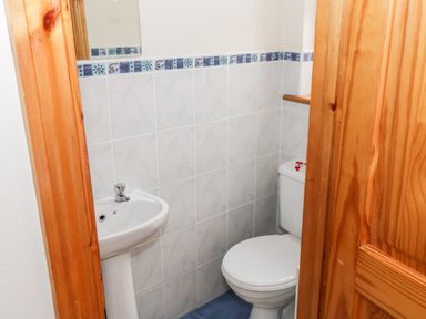 A small bathroom with a white toilet and pedestal sink with tiled walls at Lough Mask Road Fishing Cottage in Ballinrobe County Mayo